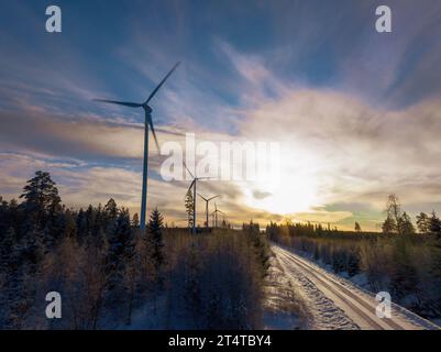 Foto aerea panoramica sulla strada invernale della foresta con mulini a vento in fila sul lato sinistro della foresta. Strada sul lato destro della vista. Foto Stock