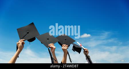 Molte mani che reggono cappelli di graduazione contro il cielo blu Foto Stock