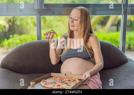 Una donna incinta si diverte a gustare una fetta di pizza, assaporando un momento di indulgenza e soddisfacendo il suo desiderio di una delizia deliziosa e confortante. Entusiasta Foto Stock