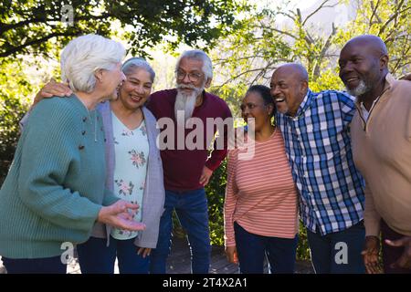 Felice e diversificato gruppo di amici anziani che si abbracciano e ridono nel giardino soleggiato Foto Stock