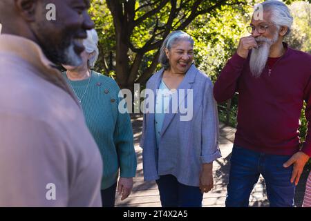 Felice e diversificato gruppo di amici anziani che discutono e sorridono nel giardino soleggiato Foto Stock