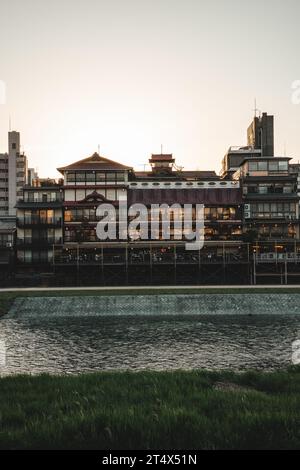 Una vista panoramica di un edificio vicino a un tranquillo lago al tramonto, con altri edifici sullo sfondo Foto Stock