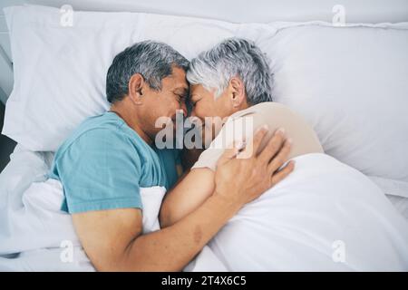 Vista dall'alto, abbraccio e coppia anziana a letto, rilassarsi e dormire con felicità, tempo di qualità e amare insieme. Romanticismo, vecchio o anziano abbraccio Foto Stock