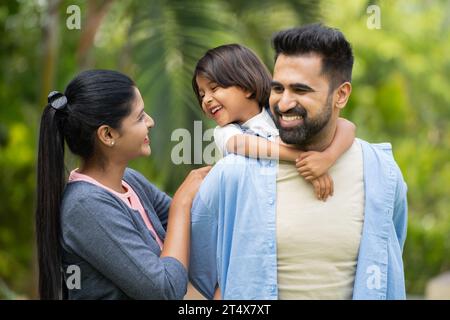 Padre indiano felice con una bambina che gioca con la madre al parco - concetto di legame familiare, genitorialità e vacanze nei fine settimana Foto Stock