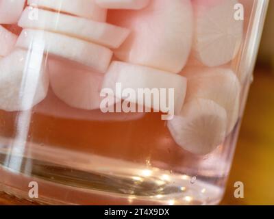 Primo piano di dischi Daikon Radish sottaceto o fette di liquido in un vaso di vetro ad angolo strano, rosa pallido dalle fette di barbabietole, sapore dolce e piccante di crostata Foto Stock