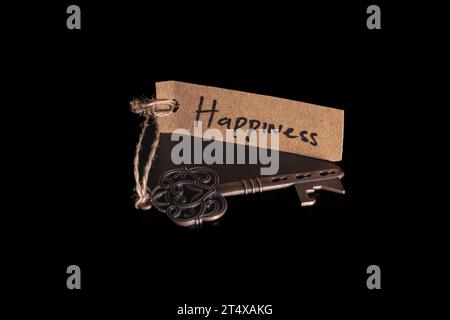 Vecchia chiave decorativa e etichetta scritta a mano "Happiness" legata con corda di paglia su sfondo nero Foto Stock