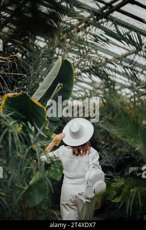 Vista posteriore di una botanica donna vestita in stile safari in piedi nella serra di palme del giardino botanico Foto Stock