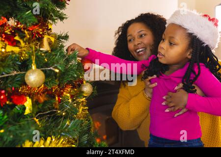 Felice madre e figlia afroamericana che decorano l'albero di natale a casa, spazio copia Foto Stock