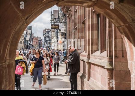 Chester, Cheshire, Inghilterra, 22 aprile 2023. Uomo che usa il telefono contro l'edificio nel centro cittadino tradizionale affollato, illustrazione di viaggio editoriale. Foto Stock