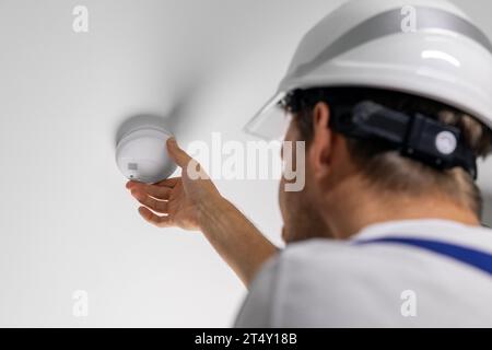 lavoratore che installa il rilevatore di fumo fotoelettrico sul soffitto dell'abitazione. sistema di sicurezza domestica e allarme antincendio Foto Stock