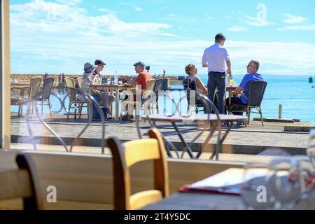 Frankreich, Omonville-la-Rogue, le Hable, 02.09.2023: Gäste des Restaurants du Port sitzen draussen im Hafen von le Hable a Omonville-la-Rogue auf der Halbinsel Cotentin an der franzoesischen Kanalkueste im Departement Manche in der Normandie *** Francia, Omonville la Rogue, le Hable, 02 09 2023 gli ospiti del Restaurant du Port si trovano all'esterno nel porto di le Hable a Omonville la Rogue sulla penisola di Cotentin sulla costa della Manica francese nel dipartimento della Manica in Normandia Foto Stock