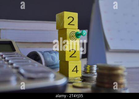 Cubo di legno con numero 2024 e pushpin circondato da soldi e calcolatrice. Obiettivo aziendale, concetto di risoluzioni finanziarie. Foto Stock