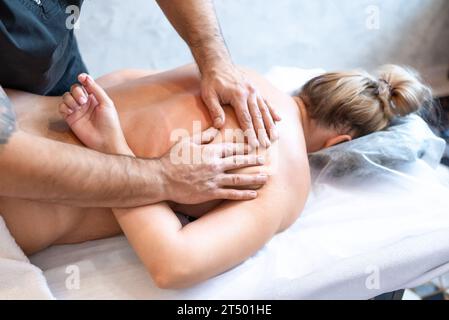 massaggiatore maschile massaggia la schiena e le spalle della donna sdraiata sul lettino da massaggio su sfondo chiaro. Il concetto di massaggi spa. Foto Stock