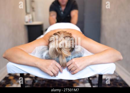 massaggiatore maschile massaggia la schiena e le spalle della donna sdraiata sul lettino da massaggio su sfondo chiaro. Il concetto di massaggi spa. Foto Stock