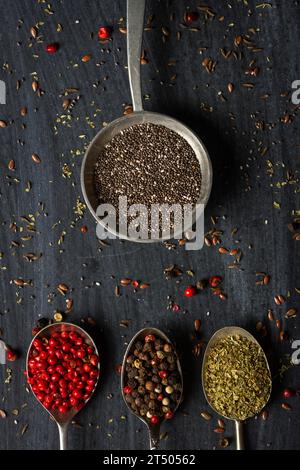 Vecchi cucchiai di metallo con diversi tipi di spezie su sfondo nero. Giacitura piatta. Vista dall'alto. Concetto di cibo. Fotografia di cibo di umore scuro. Foto Stock