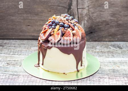 Deliziosa torta con fichi immersi nel cioccolato fuso, noci pecan, uva, morsi al cioccolato e biscotti in cima. Concetto di torta autunnale o estiva Foto Stock