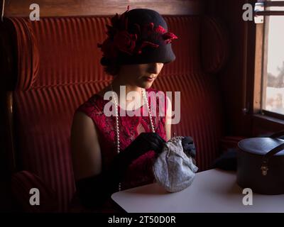 Attraente donna 1920s in abito flapper rosso e cappello di cloche posa nel 1927 prima classe interno di un autentico treno a vapore Foto Stock