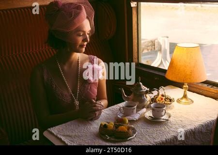 Scena di rievocazione di una donna di vestito flapper 1920s godendo di tè in un autentico compartimento del treno a vapore 1927 Foto Stock