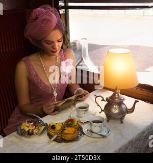 Scena di rievocazione di una donna di vestito flapper 1920s godendo di tè in un autentico compartimento del treno a vapore 1927 Foto Stock