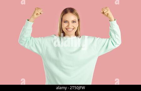 Una donna bella sicura e forte che scherzosamente alza le braccia e mostra i suoi muscoli. Foto Stock