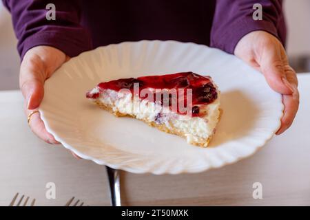 mani che reggono la cheesecake con condimento di ciliegia e sfondo di legno Foto Stock