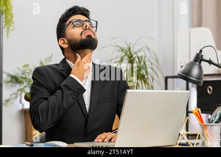 Uomo d'affari indiano libero professionista che si sente male malato malato affetto da mal di gola ferito deglutizione dolore tocca il collo lavorare a casa ufficio sul posto di lavoro. Maschio arabo in tuta formale ha un raffreddore, influenza, virus Foto Stock