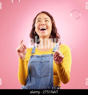Felice, donna e gioca con Bubbles in studio, sfondo rosa ed entusiasta di celebrare la libertà. Asiatico modello femminile pop liquido sapone bolla per divertimento Foto Stock