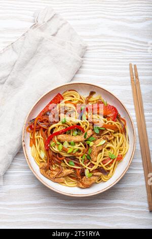 Ciotola bianca con Chow Mein o lo Mein, spaghetti tradizionali cinesi con carne e verdure, serviti con bacchette e vista dall'alto su rustico bianco Foto Stock