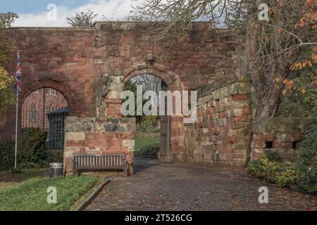 Porta d'ingresso con due archi che conducono a un giardino con panca da giardino, palo da bandiera e bandiera union Jack Foto Stock