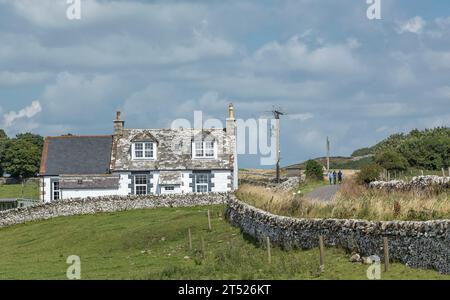 Cottage scozzese con pareti e tetto ricoperti di licheni e una corsia e gli escursionisti che camminano lungo la strada Foto Stock