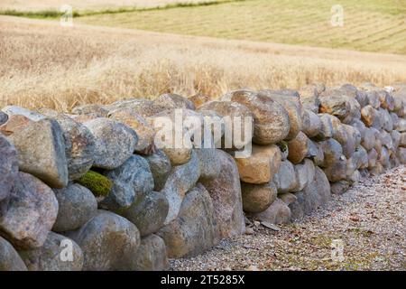 Un vecchio muro di roccia in una fattoria all'aperto in una giornata di sole, separando le colture con una struttura artificiale. Barriera in pietra nel design dell'architettura rurale e. Foto Stock