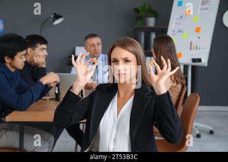 Giovane donna d'affari con tappi per le orecchie che soffre di colleghi rumorosi in ufficio Foto Stock