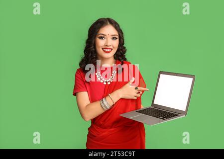 Bella donna indiana in sari che punta il laptop su sfondo verde Foto Stock