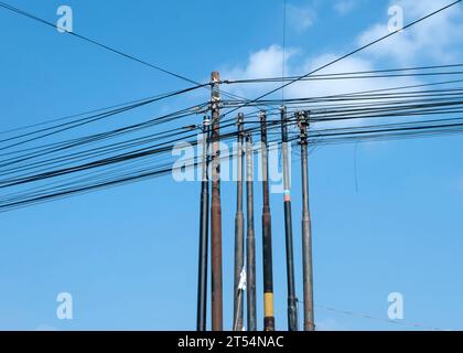 Molti cavi di comunicazione Internet in fibra su pali a Yogyakarta, Indonesia, con sfondo blu. Foto Stock