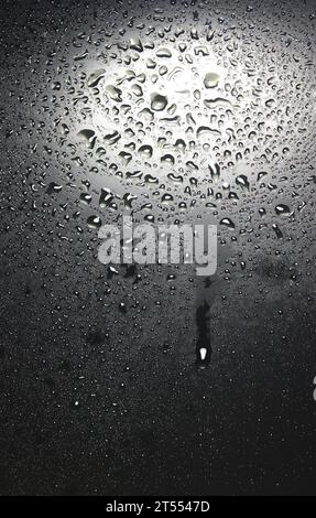 Struttura a griglia quadrata sottile in gocce d'acqua su sfondo verticale superficie nero opaco Foto Stock