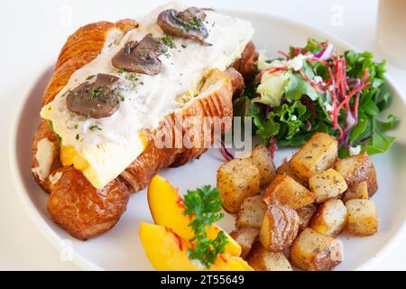 Panino brioche con brioche di uova strapazzate con pesche, feta con foglie di rucola e patate saltate. Foto Stock