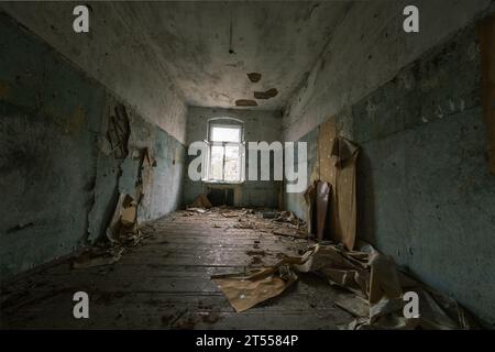 L'interno della camera abbandonata con pareti dipinte che si staccavano danneggiava la spazzatura dei mobili di legno sul pavimento sporco con soffitto sgretolato che mostrava aste di ferro Foto Stock
