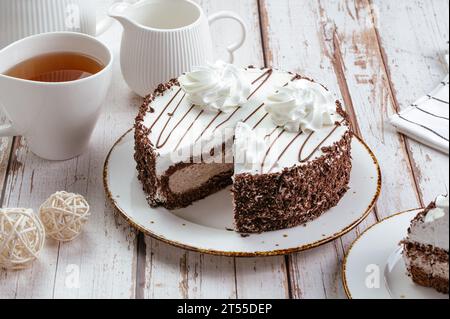 torta al cioccolato con panna su un piatto, tè in tazza, sfondo chiaro Foto Stock
