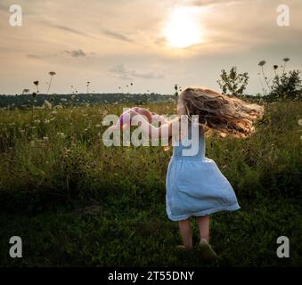 Bambina con lunghi ricci biondi che girano in abito all'aperto Foto Stock