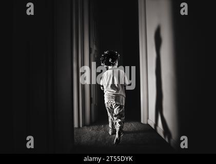 Bambino che cammina lungo il corridoio buio indossando i curvilini Foto Stock
