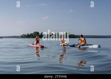 Amici che bevono birra durante le vacanze estive sul lago, paddleboard. Foto Stock