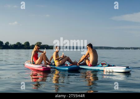 Amici che bevono birra durante le vacanze estive sul lago, paddleboard. Foto Stock