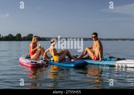 Amici che bevono birra durante le vacanze estive sul lago, paddleboard. Foto Stock