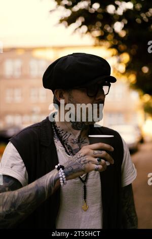 L'uomo bello ed elegante beve caffè, le sue mani sono coperte di tatuaggi. Foto Stock