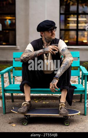 L'uomo bello ed elegante beve caffè, le sue mani sono coperte di tatuaggi. Foto Stock
