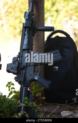 arma nera nell'ombra accanto a uno zaino nero, equipaggiamento airsoft Foto Stock