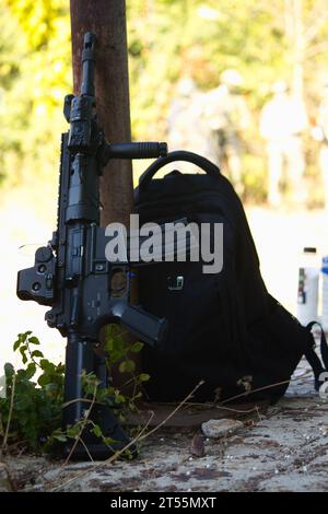 arma nera nell'ombra accanto a uno zaino nero, equipaggiamento airsoft Foto Stock