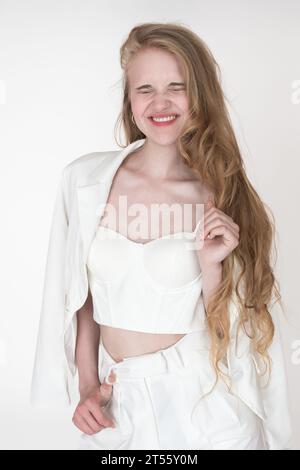 Espressione facciale positiva di una donna bionda con gli occhi chiusi e sorriso toothy ridendo. Felicità donna caucasica ben vestita Foto Stock