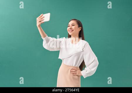 Giovane ragazza sorridente che scatta selfie su smartphone su sfondo verde Foto Stock