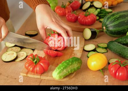 Pomodori grandi maturi, melanzane, verdure su un locale di lavoro in legno della cucina. Molte verdure crude di fondo. Pomodoro, cetrioli. Fornello a casa che fa una h Foto Stock